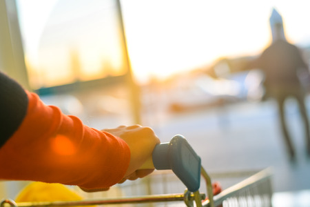 Hand with shopping cart near a car parking at sunset backgroundの写真素材