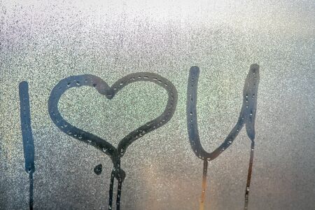 Closeup on I love you sign drawing on fogged window glass background