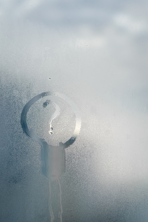 Drawing of question mark and lamp icon inscription on foggy window glass. Idea or ecology conceptの写真素材