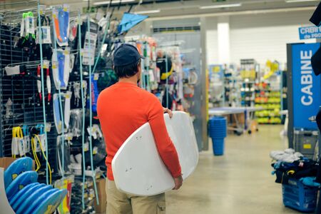 Man choosing and holding a white surf board on shop background indoors