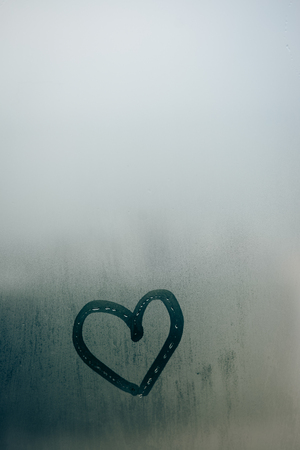 Love heart painted on glass. The window is fogged up with drops on the backgroundの写真素材