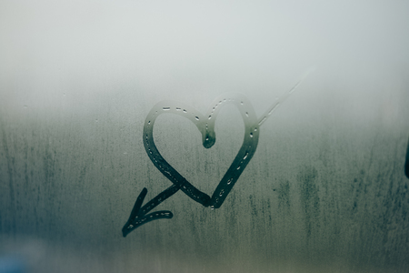 Love heart with arrow on a wet window. Closeup on foggy glass backgroundの写真素材