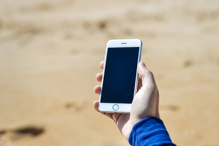 Top view shot of a man's hand holding a smartphone on the beach backgroundの写真素材