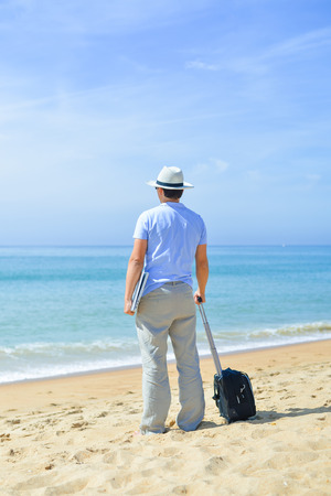 Back view of young businessman with laptop on the beach blue sky outdoors background. Arriving at dream holiday destinationの写真素材