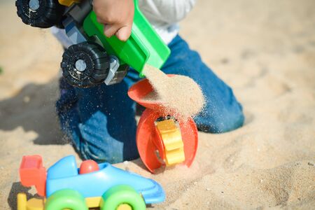 Child playing with toys on sunny summer day sandy background. Kid having fun outdoors.