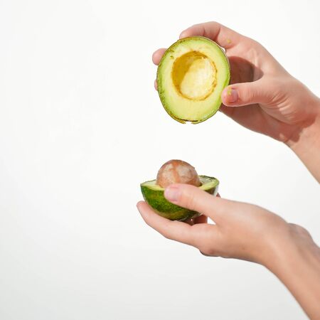 Closeup on hands holding fresh avocado cut in half on light background