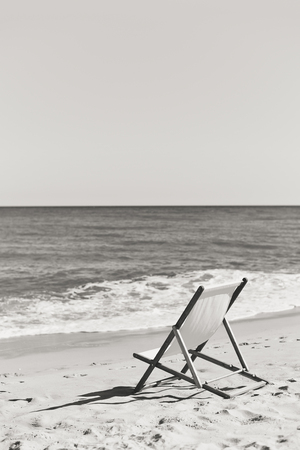 Black and white picture back view of deckchair on a beach, sunny ocean sky background outdoors