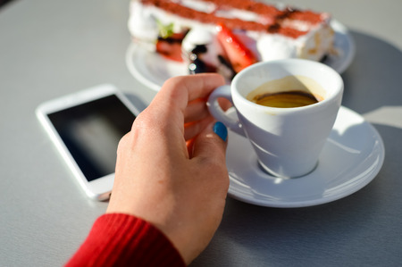 Top point of view on hand with smartphone, coffee and cake at restaurant backgroundの写真素材