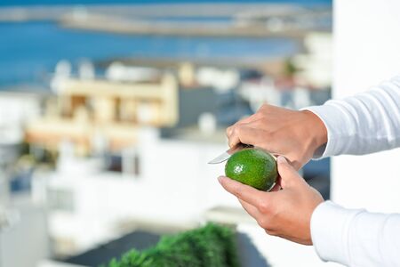 Hands holding knife and cutting fresh avocado in half on light blue background. Closeupの写真素材