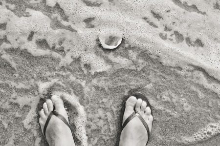 Black and white photo of beach outdoors background - feet in flip flops. Summer vacation idea