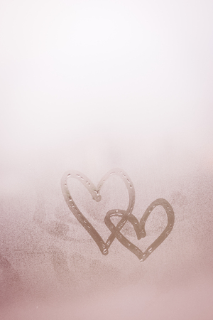 Love heart couple symbol drawn by hand on the wet frozen window glass with sunlight background. Close upの写真素材