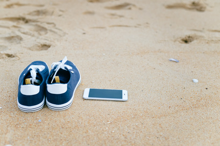 Sport shoes and mobile smart phone on holiday, closeup. Touchscreen device technology on vacationの写真素材