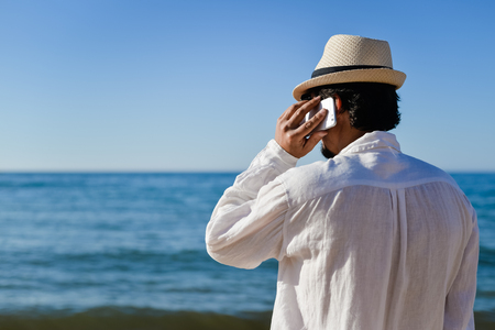 Back side view of man talking on smart phone, vacation beach backgroundの写真素材