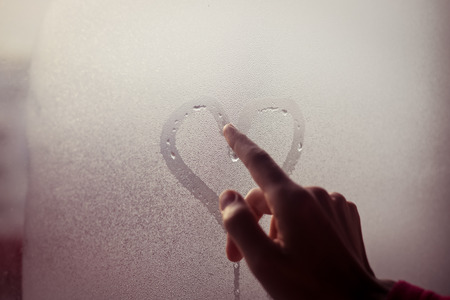 Person drawing heart with finger on wet windowの写真素材