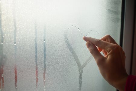 Person drawing love heart with finger on wet window background