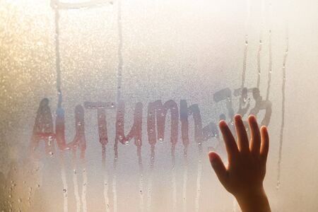 Autumn written and child hand on fogged window, close up sign. Drops of rain on glass backgroundの写真素材