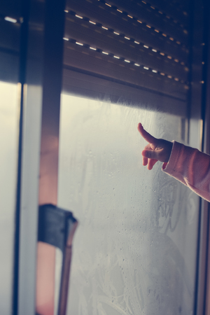 Child hand drawing on fogged glass looking through the window, closeupの写真素材