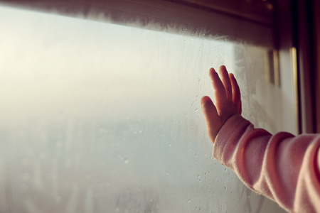 Closeup on child hand on fogged glass looking through the window,の写真素材