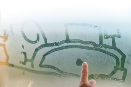Child hand draws on fogged window, close up sign. Drops of rain on glass backgroundの写真素材