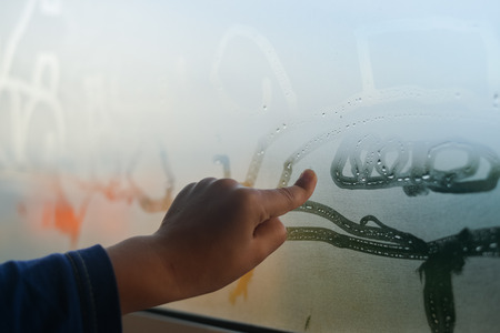 Child hand draws on fogged window, close up sign. Drops of rain on glass backgroundの写真素材
