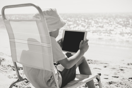 Child using playing tablet computer on the beach sunny outdoors backgroundの写真素材