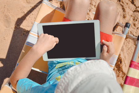 Child using playing tablet computer on the beach sunny outdoors background. Top view mock up styleの写真素材