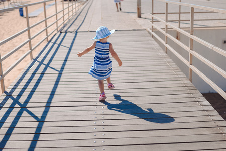 Back view of little baby girl walking on a wooden pathway sunny outdoors backgroundの写真素材