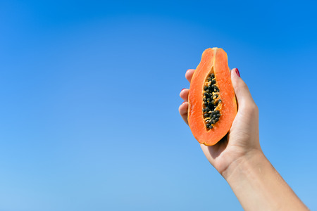Close up on person hand holding a half papaya fruit on sunny blue sky backgroundの写真素材
