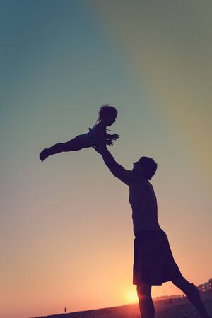 Silhouette of happy family, joyful father throwing up his child in the park on the sunset sky outdoors backgroundの写真素材