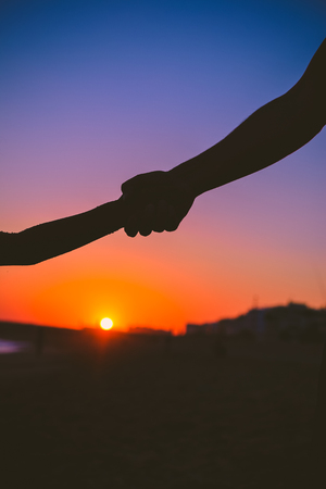 Closeup view of child and adult hands on sunset outdoors background.の写真素材