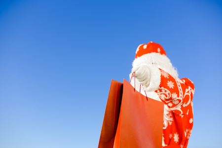 Merry Christmas with joyful Santa Claus ready to ship and delivering gift shopping bag on sunny blue sky outdoors background. Happy time for amazement and excitementの写真素材