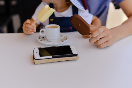 Closeup on family holding eating ice cream, using mobile phone on table background. Mock up style top viewの写真素材
