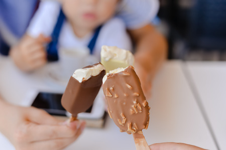 Closeup on family holding eating ice cream, using mobile phone on table background. Mock up style...