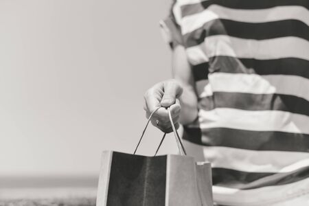 Black and white closeup on person hand holding paper bag with handles, light backgroundの写真素材