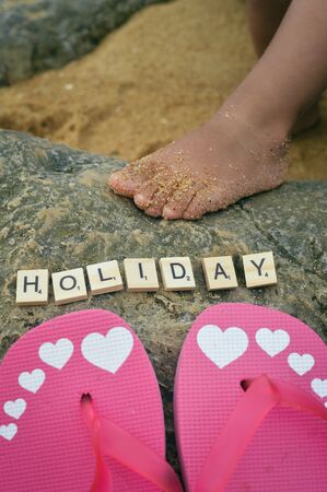 Holiday sign, child foot and adult flip flops resting on the beach background, top view flat lay closeupの写真素材
