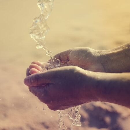 Closeup on hands holding water, sunny day beach outdoors backgroundの写真素材
