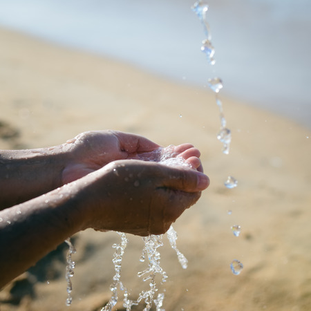 Closeup on hands holding water, sunny day beach outdoors backgroundの写真素材
