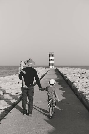 Black and white back view of male with kids walking to the red lighthouse, sunny outdoors backgroundの写真素材