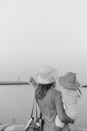 Black and white back view of mather and child finger pointing looking at sky, lighthouse at sunset, dawn outdoors backgroundの写真素材