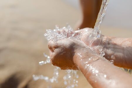 Person holding hands in splashing water, sunny sandy outdoors background