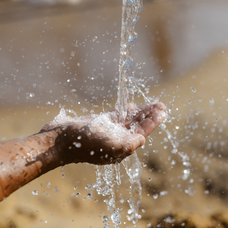 Closeup on human hand catching water, sunny summer outdoors backgroundの写真素材