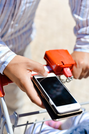 Person order buying via smart phone application, shop cart department store mall background. Closeup top view mock up background photoの写真素材