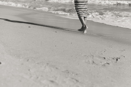 Black and white image of person walking by the shore in the beach, sunny outdoors sandy backgroundの写真素材