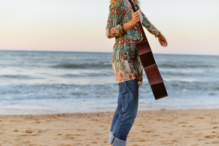 Fragment of a beautiful female playing guitar on the beach, sunset sunny blue sky outdoors backgroundの写真素材