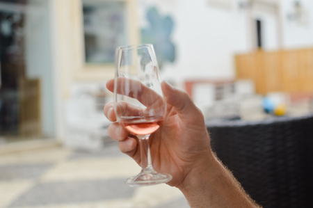 Closeup on human hand holding wine glass, bar restaurant terrace on backgroundの写真素材