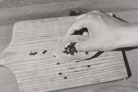 Black and white image closeup on hand holding ripe half papaya on table backgroundの写真素材
