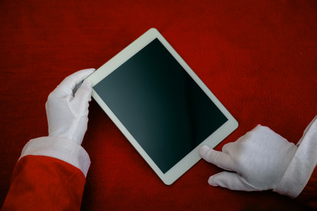 Joyful Christmas online shopping. Closeup on Santa Claus working using mobile tablet computer on table background. Social network, electronic commerce, banking, logistic operations, resolutionの写真素材