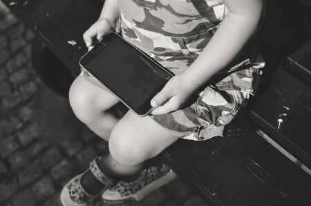 Top view on little child sitting using smartphone holding in handsの写真素材