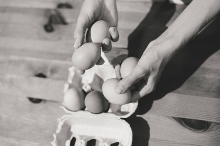 Black and white image of hand holding chicken eggs in a cardboard box on table background. Flat lay...
