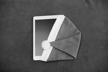 Mock up flat lay of tablet pc computer with Santa hat on table fabric texture background surface. Close up top view designの写真素材